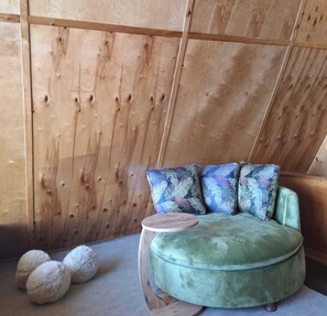 Una habitación con un sofá verde, dos cojines estampados, una pequeña mesa de madera y tres cojines redondos en el suelo.