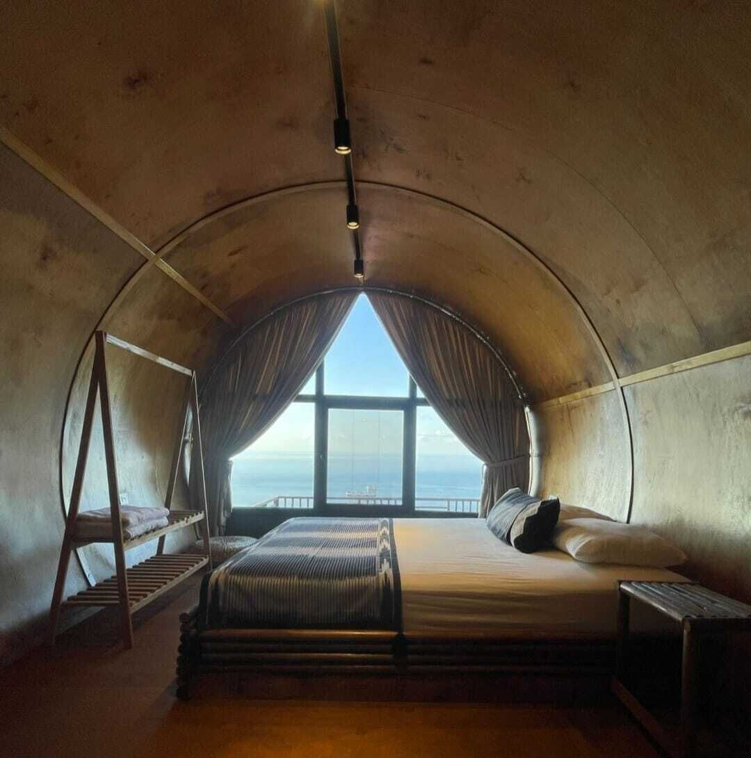 Une pièce circulaire et accueillante, avec un lit, un banc et une fenêtre donnant sur la mer.