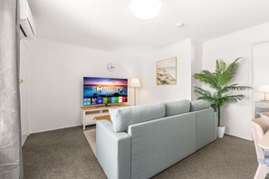 A modern living room with a grey sofa, a flat-screen TV, a potted plant, and a painting on the wall. - Peaceful 1-bed Apartment in Kedron With Parking (Brisbane)