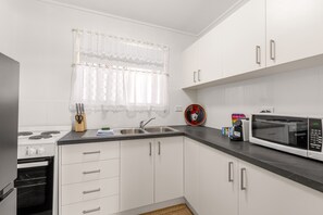 A kitchen with white cabinets, a stainless steel sink, a microwave, and a stove. - Peaceful 1-bed Apartment in Kedron With Parking (Brisbane)