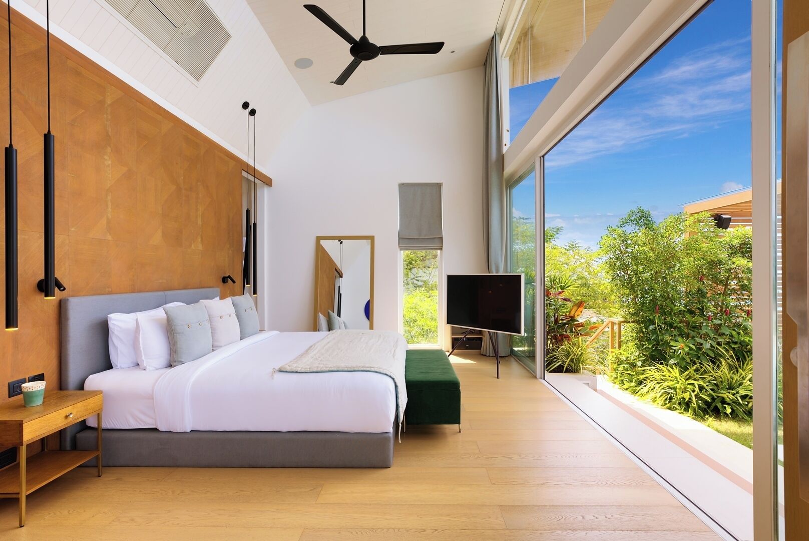Een moderne slaapkamer met een groot bed, een flatscreen televisie en uitzicht op groen.