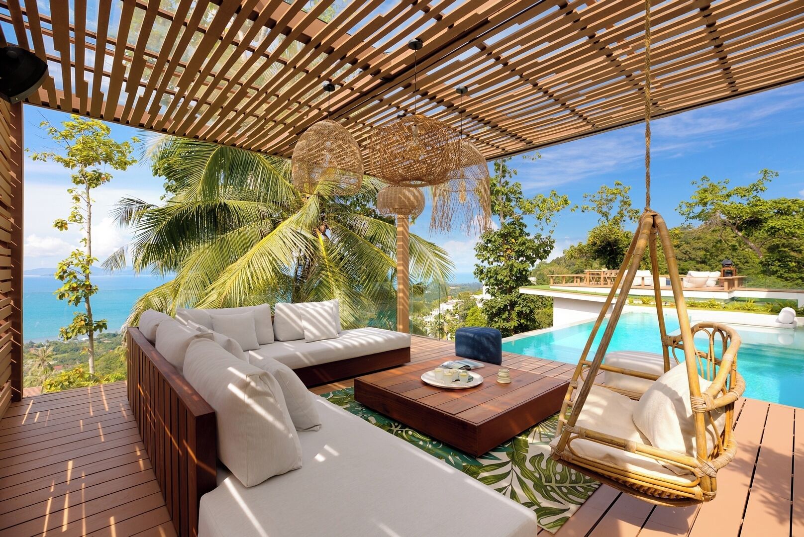 En træterrasse med en sofa og hængekøjsstol med udsigt over pool og hav.