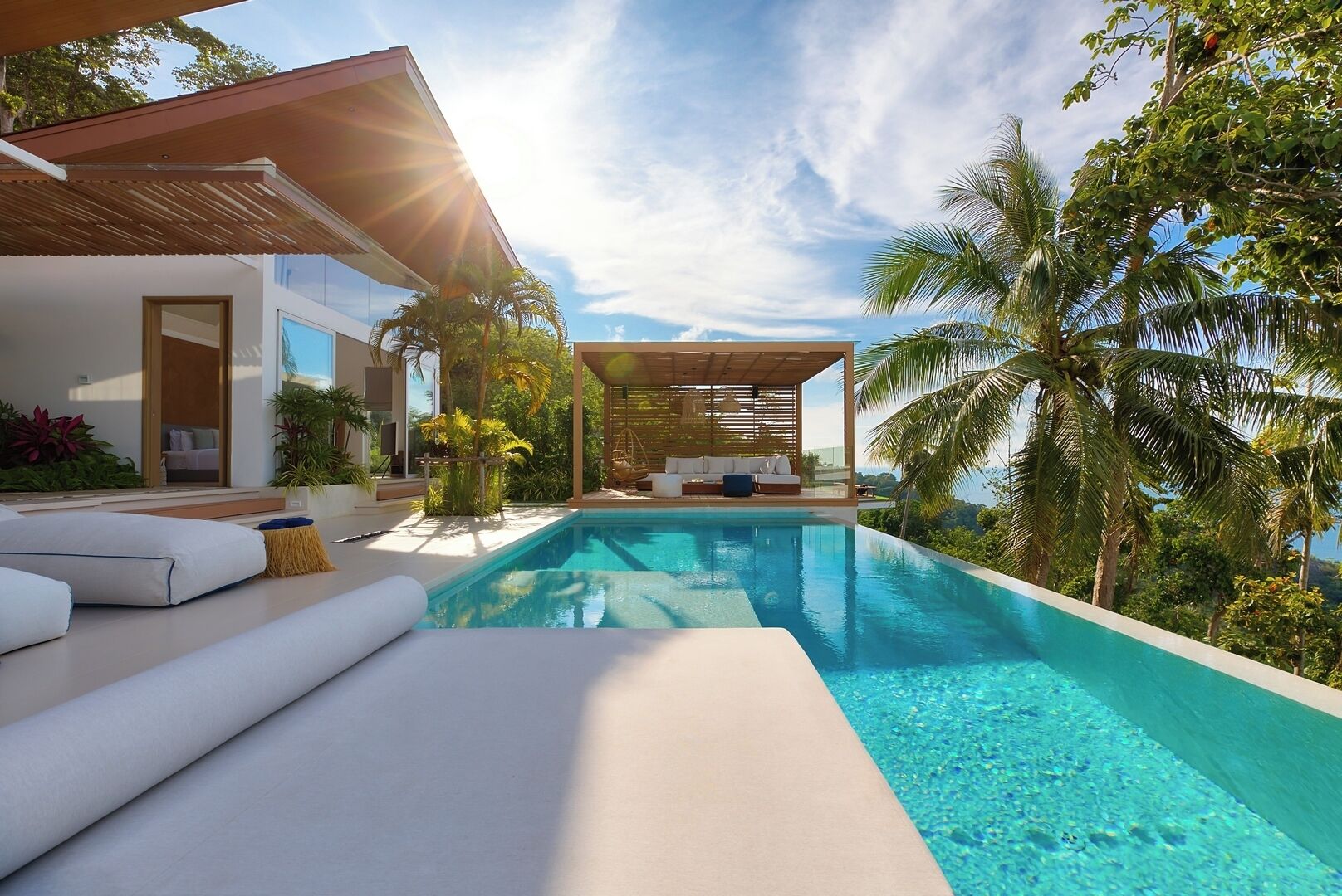Ein moderner Poolbereich mit freiem Blick auf den Pool, einer überdachten Lounge-Ecke und üppiger Bepflanzung.