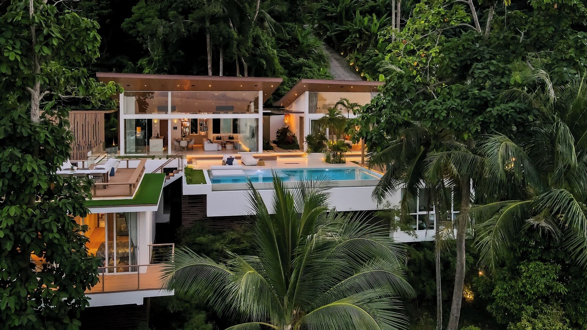A modern house with a pool, surrounded by lush greenery.