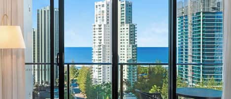 A room with a large window offering a view of tall buildings and the ocean.