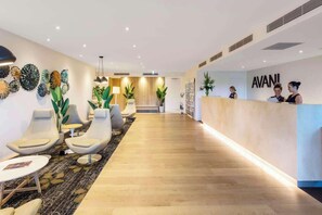 Un hall d’accueil d’hôtel avec un plancher en bois, des chaises modernes et un comptoir de réception orné d’un logo.