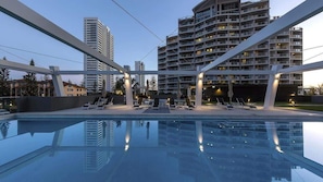 Ein Pool mit Liegestühlen und Sonnenschirmen, umgeben von modernen Gebäuden.