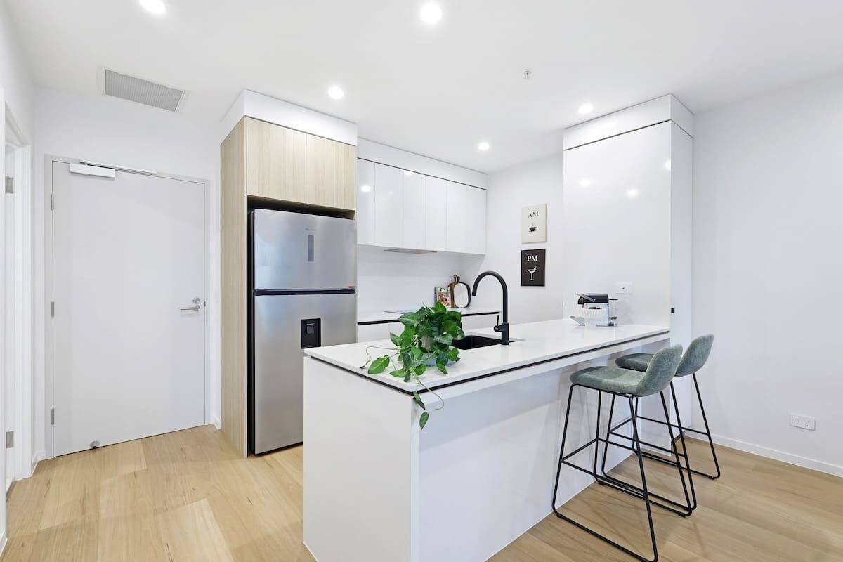 A modern kitchen with white cabinetry, a stainless steel refrigerator, a sink, and bar stools.
