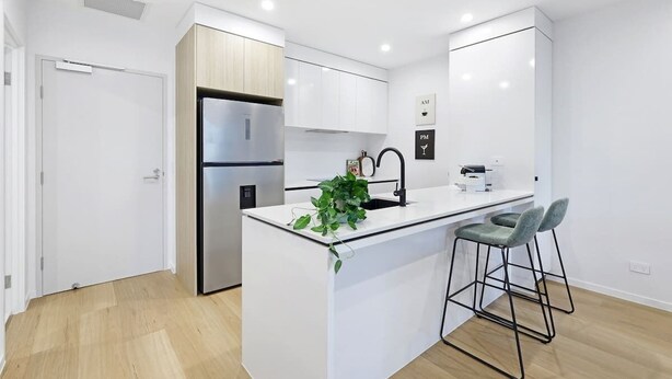 A modern kitchen with white cabinetry, a stainless steel refrigerator, a sink, and bar stools. - Riverfront 2BR | Pool + Gym | Surfers (Surfers Paradise)