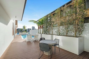 A wooden deck with a pool, chairs, and a table. - Riverfront 2BR Surfers Paradise Apt, Pool, Gym & Free Parking (Surfers Paradise)