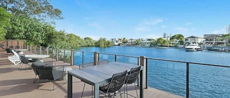 A deck with outdoor seating overlooking a body of water, with buildings in the background.