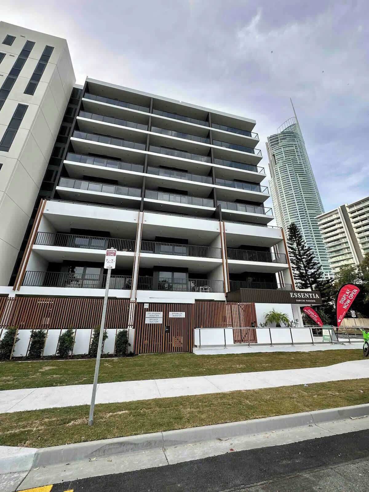 A multi-story building with a modern architectural design, featuring balconies and a gated entrance.