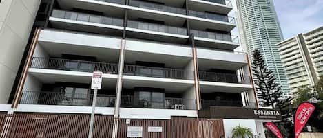 Un edificio de varios pisos con diseño arquitectónico moderno, que cuenta con balcones y una entrada con portón.