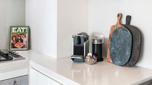 A kitchen counter with a coffee maker, a mug, a frying pan, and a framed picture. - Ocean & River Views | Sauna + Steam Rm (Surfers Paradise)