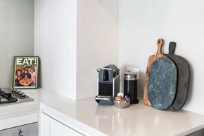 A kitchen counter with a coffee maker, a mug, a frying pan, and a framed picture. - Ocean & River Views | Sauna + Steam Rm (Surfers Paradise)