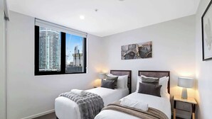 A hotel room with two beds, a large window with a city view, and a framed artwork on the wall. - Ocean & River Views | Sauna + Steam Rm (Surfers Paradise)