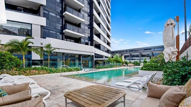 A modern hotel with a swimming pool, outdoor seating, and lush greenery. - Ocean & River Views | Sauna + Steam Rm (Surfers Paradise)