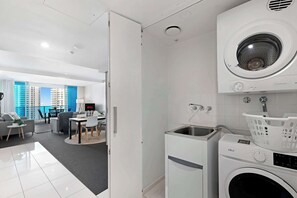 A modern apartment with a dining area, a laundry room with a washing machine and dryer, and a view of a cityscape through large windows. - 2BR Ocean View Hilton | Kids' Pool, Gym, Parking (Surfers Paradise)