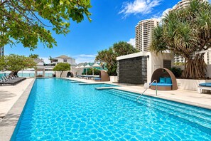 A swimming pool with lounge chairs and a stone wall. - Hilton 2BR Ocean Views, Pool+slide, Gym & Parking (Surfers Paradise)