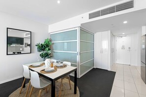 A modern dining area with a white table set for four, a large mirror, and a plant. - 2BR Ocean View Hilton | Kids' Pool, Gym, Parking (Surfers Paradise)