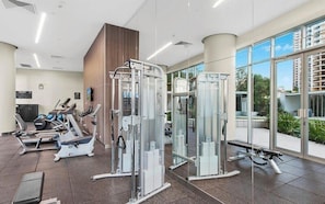 A gym with various exercise machines, a large window, and a view of buildings outside. - 2BR Ocean View Hilton | Kids' Pool, Gym, Parking (Surfers Paradise)
