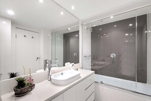 A modern bathroom with a large mirror, a white sink, and a glass-enclosed shower area. - Hilton 2BR Ocean Views, Pool+slide, Gym & Parking (Surfers Paradise)
