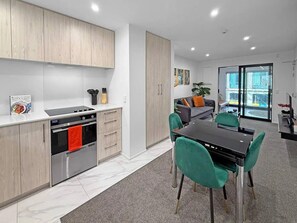 A modern kitchen with a built-in oven and a dining area with a black table and green chairs.