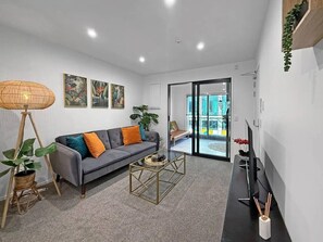 Una sala de estar moderna con un sofá gris, una mesa de centro de cristal y un televisor sobre un mueble negro.