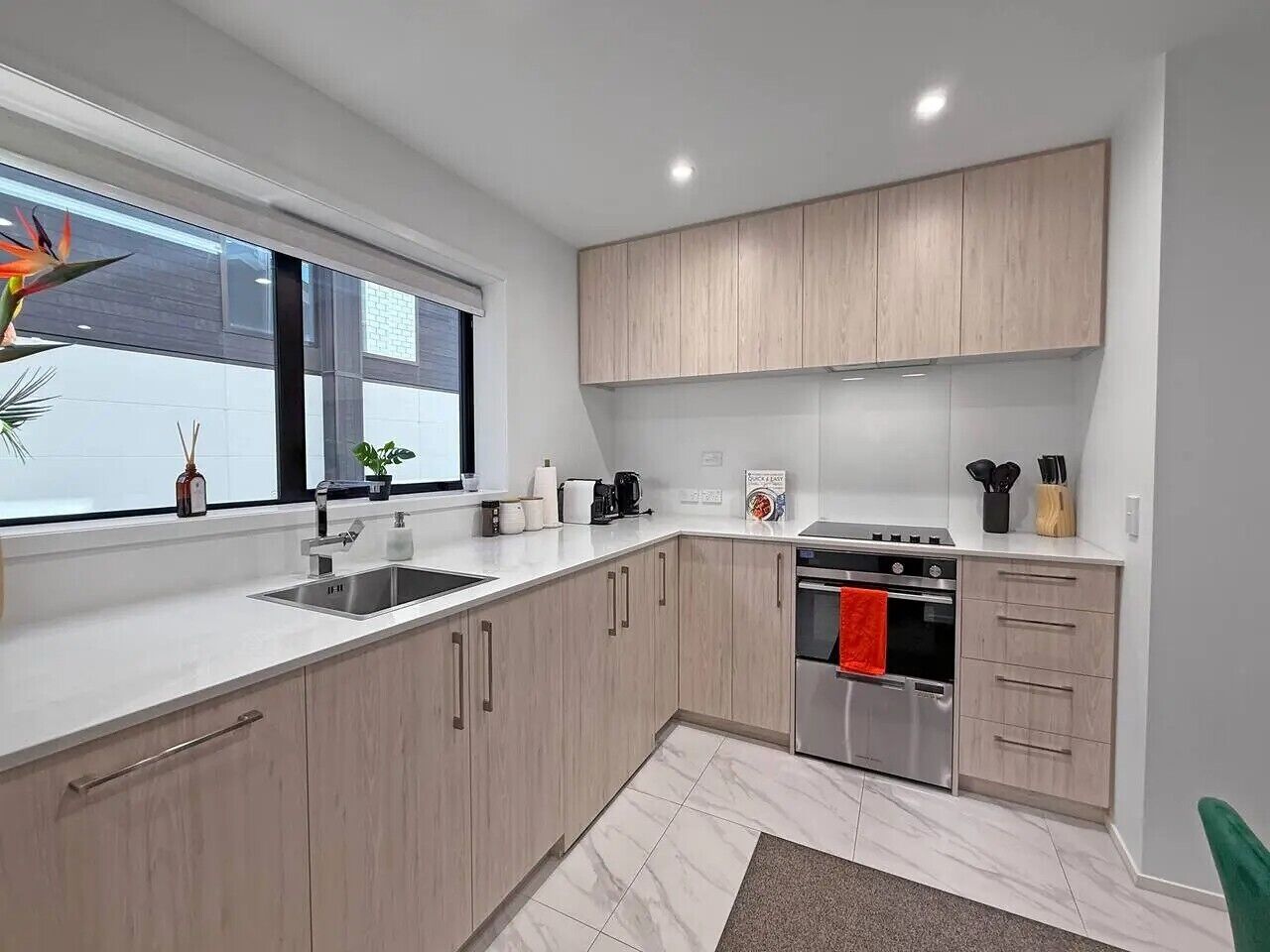 A modern kitchen with light wood cabinets, a stainless steel stove, and a window with a view.
