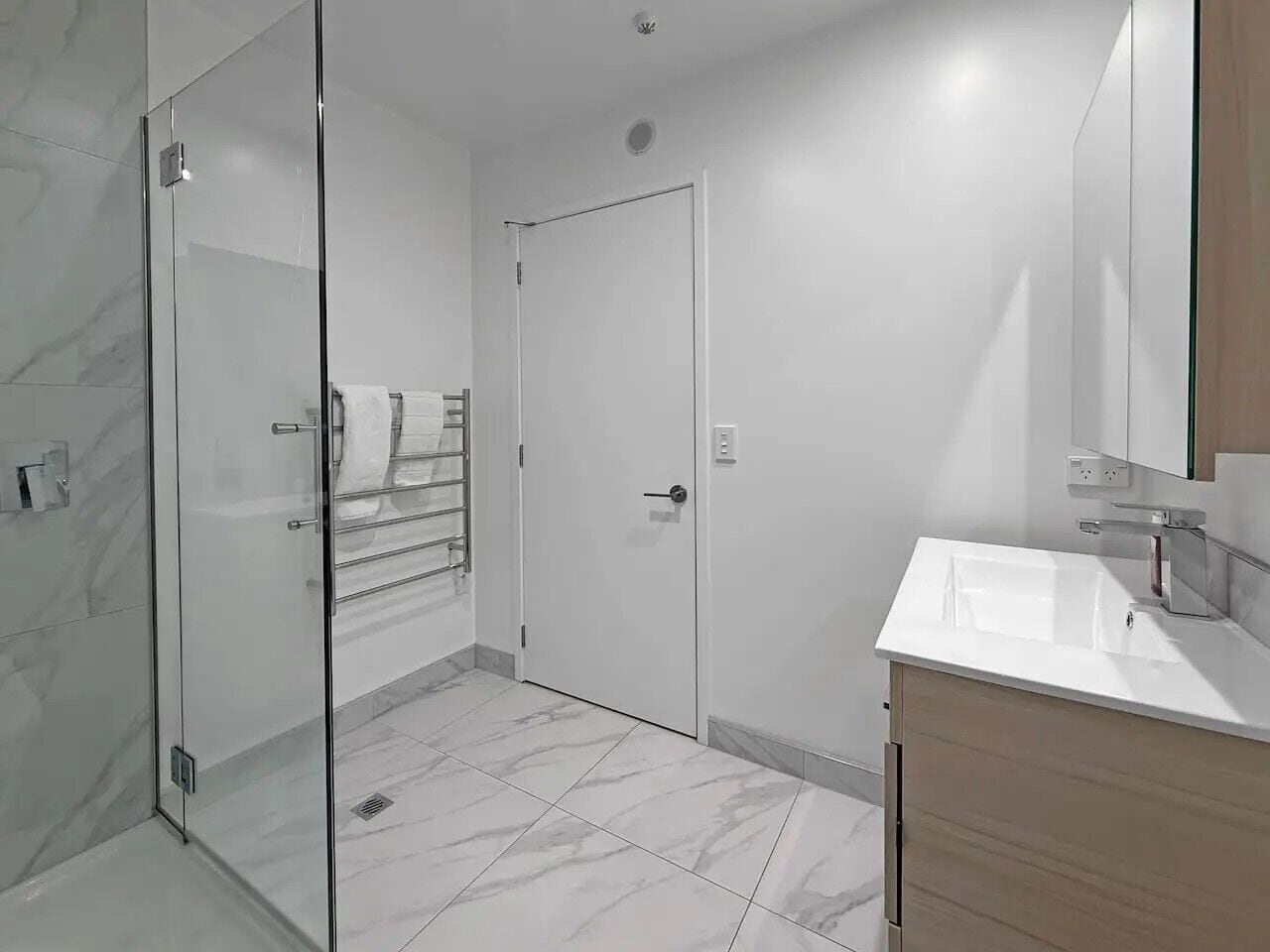 A modern bathroom with a glass shower enclosure, a white sink, and a wooden vanity.