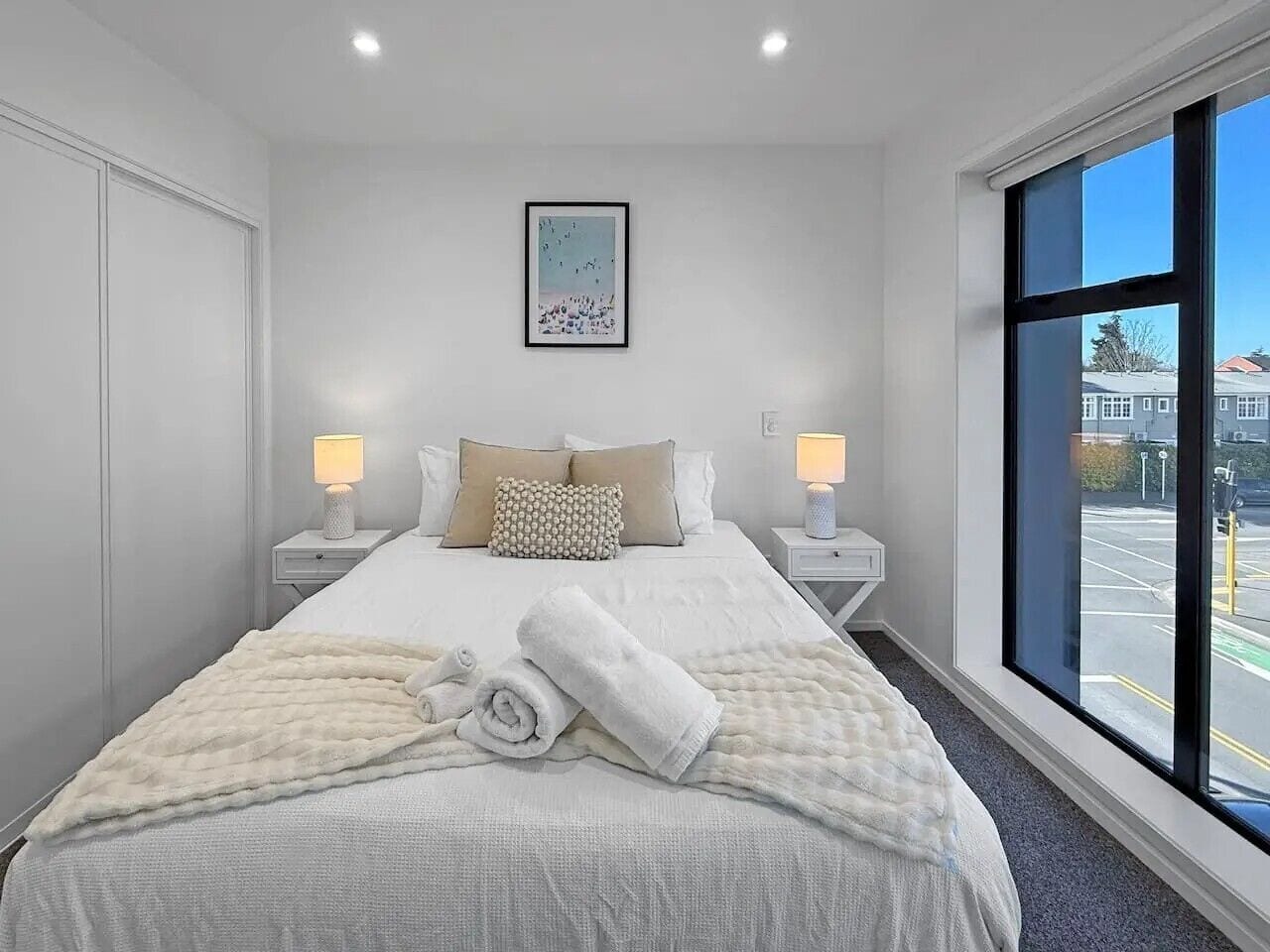 Ein Hotelzimmer mit einem großen Bett, zwei Nachttischen, einem Fenster mit Blick und einem gerahmten Bild an der Wand.