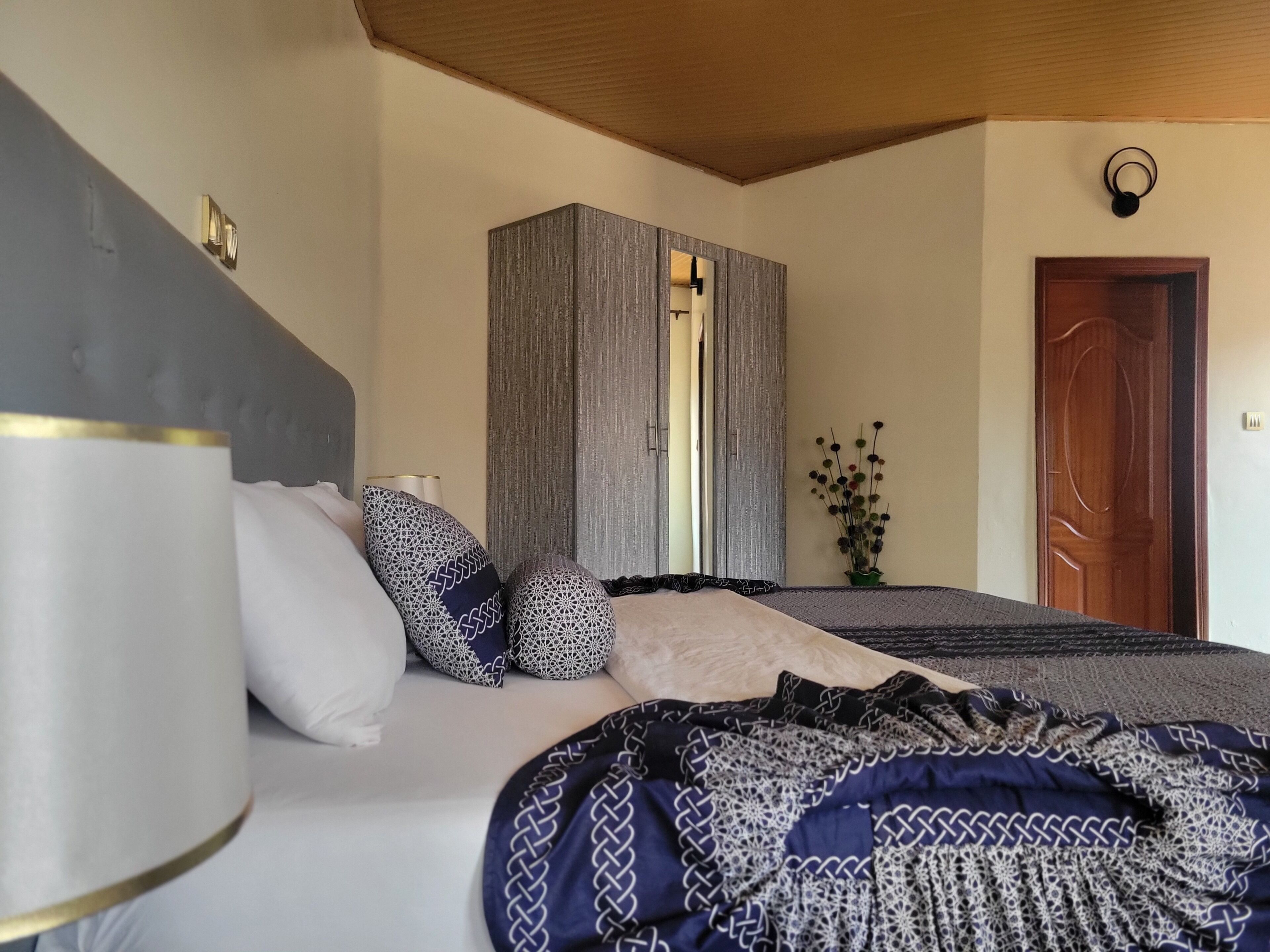 Un dormitorio con cama, almohadas, una lámpara de noche, armario y una puerta.