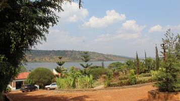 A view of a lake with a hilly landscape in the background, surrounded by lush greenery and a few parked cars.