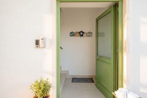 A hallway with a green door, a wall-mounted intercom, a doormat, and a small potted plant. - ALL BlueNote – 2 Bedrooms, 2 Baths & Stunning Sea Views (Polignano a Mare)