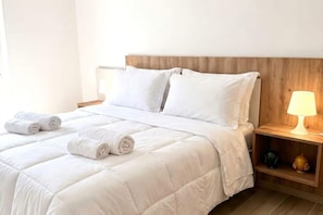 A neatly made bed with white bedding and rolled towels, a wooden headboard, and a bedside table with a lamp. - ALL BlueNote – 2 Bedrooms, 2 Baths & Stunning Sea Views (Polignano a Mare)