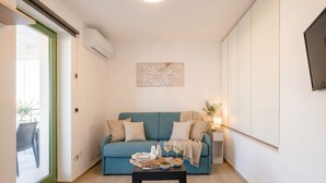 Uma sala de estar moderna com um sofá verde-água, uma mesa de centro com petiscos e bebidas, e uma vista através de uma porta de vidro.