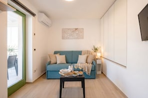 A modern living room with a teal sofa, a coffee table with snacks and drinks, and a view through a glass door. - ALL BlueNote – 2 Bedrooms, 2 Baths & Stunning Sea Views (Polignano a Mare)