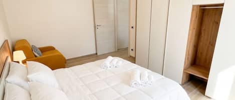 A hotel room with a bed, a wooden bench, a wardrobe, and a door.