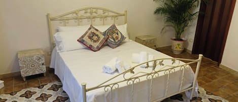 A neatly made bed with decorative pillows, a bedside table, a potted plant, and a patterned rug.