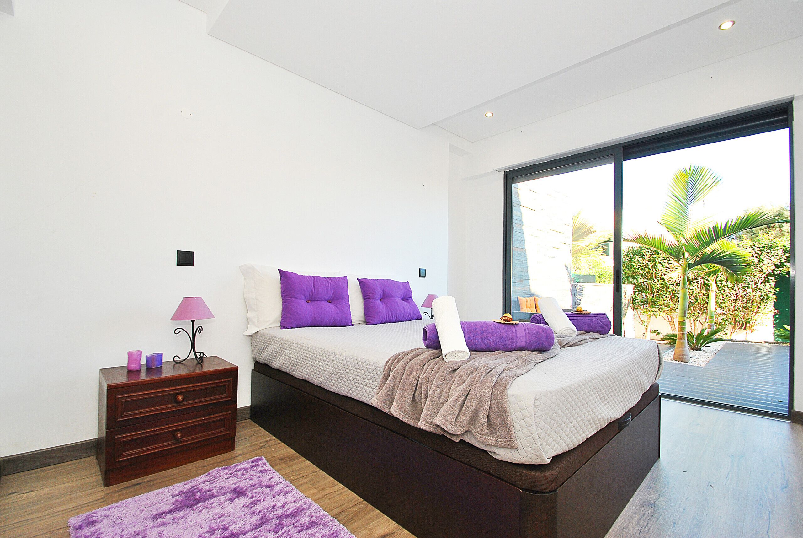 A bedroom with a large bed, a nightstand, a lamp, and a view of the outdoors.