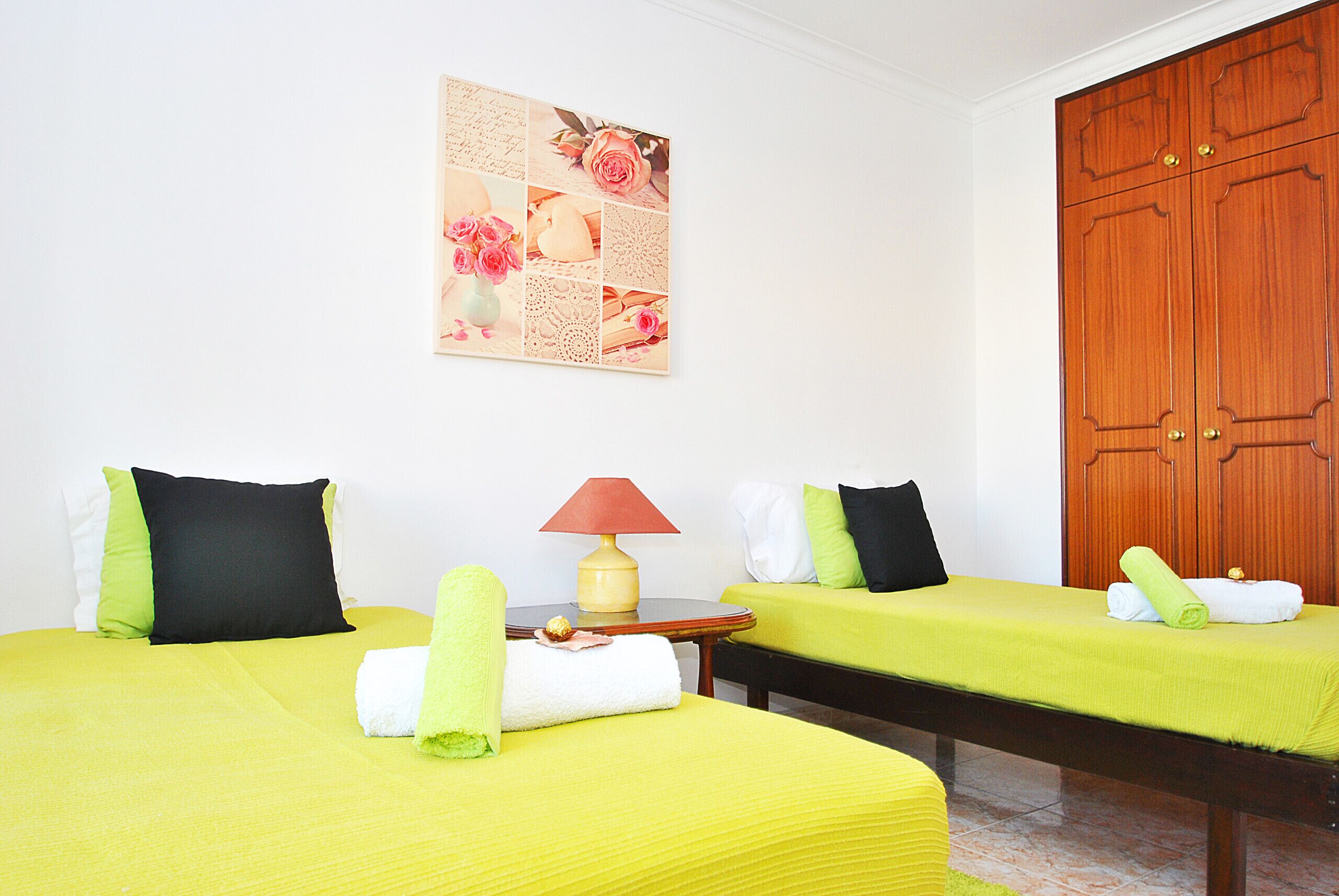 A hotel room with two beds, a small table with a lamp, and a wooden wardrobe.