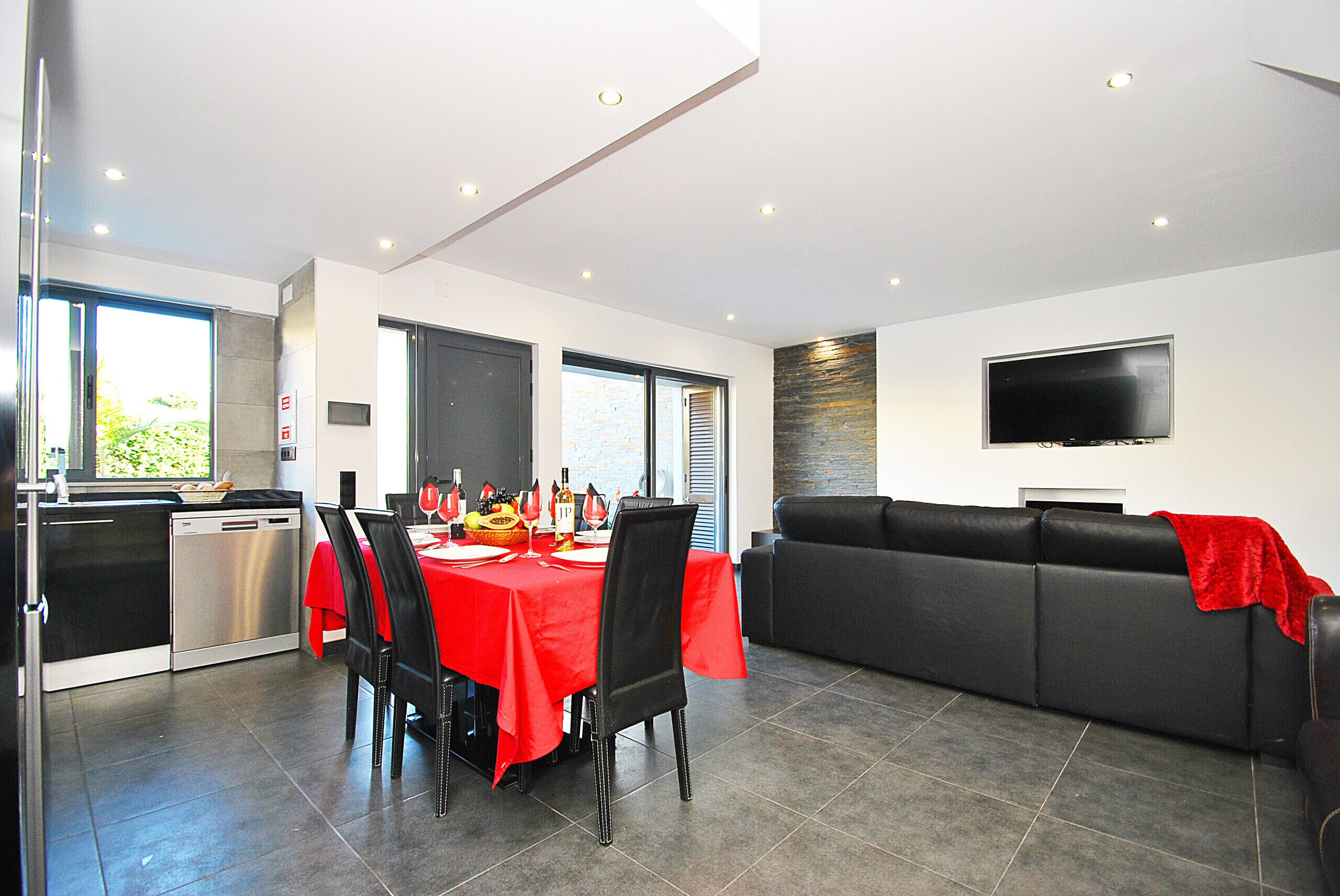 A modern dining area with a red table, black chairs, and a black sofa with a red throw.