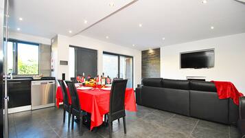 A modern dining area with a red table, black chairs, and a black sofa with a red throw.