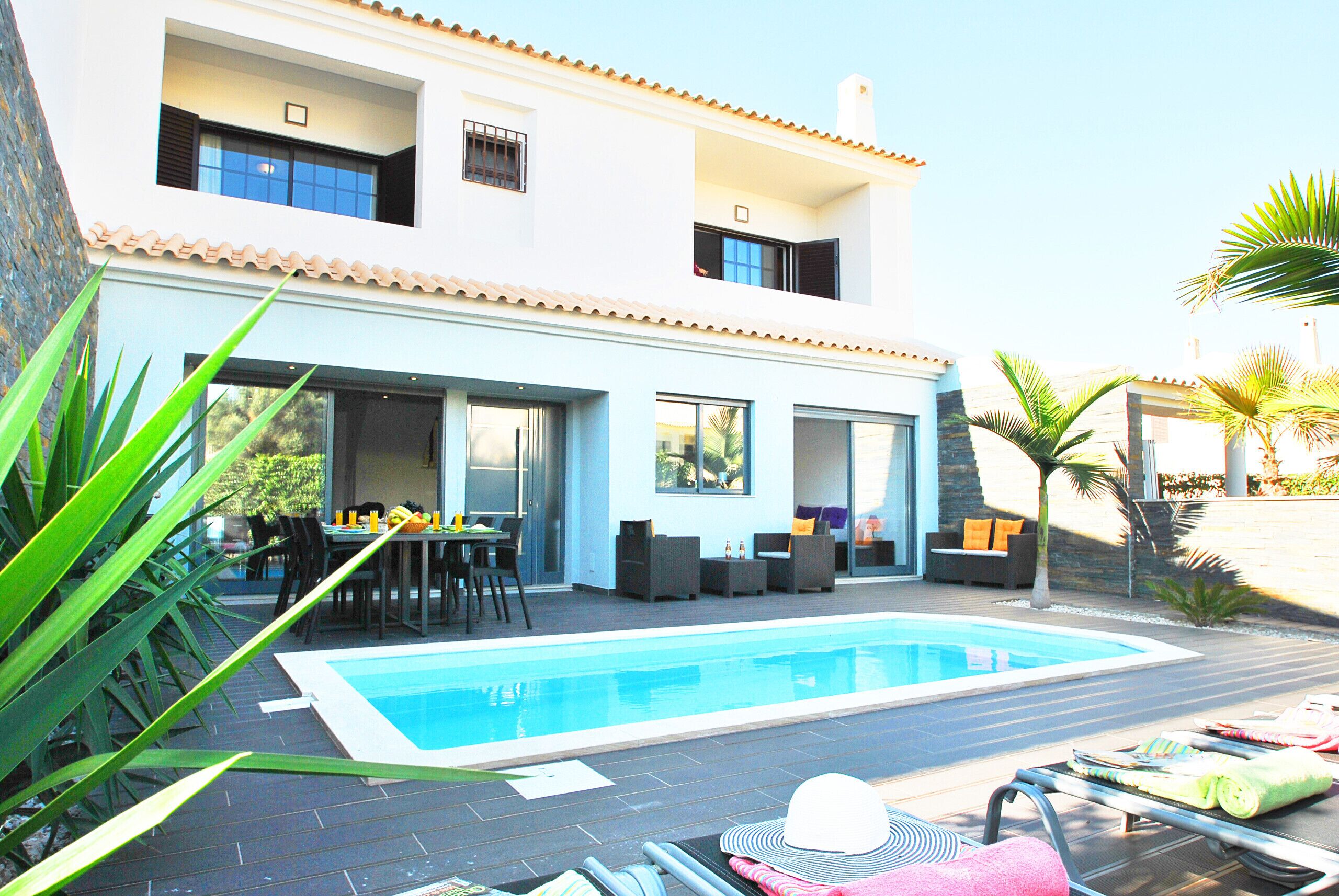 A two-story house with a swimming pool, outdoor seating, and a dining area.
