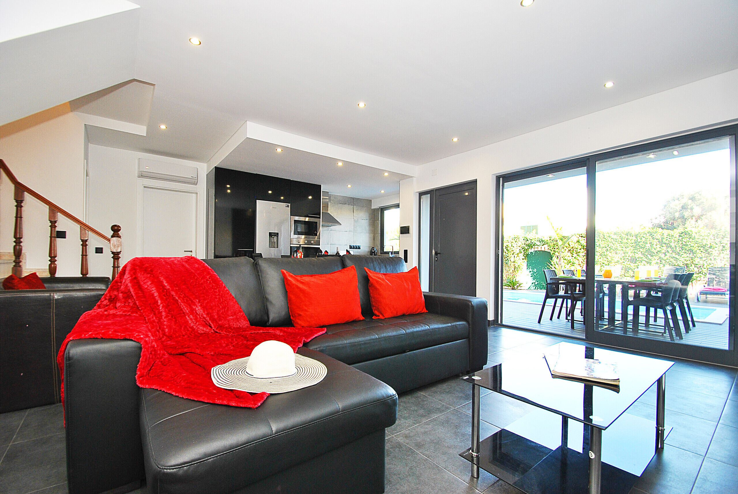 Una sala de estar moderna con un sofá de cuero negro, cojines rojos y una zona de comedor con mesa de vidrio.