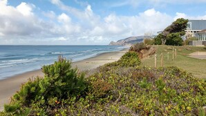 A coastal landscape with a beach, vegetation, and a building with a modern design. - Oceanfront Home with Sweeping Pacific Views (Lincoln City)