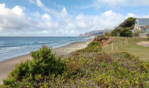 A coastal landscape with a beach, vegetation, and a building with a modern design. - Oceanfront Home with Sweeping Pacific Views (Lincoln City)