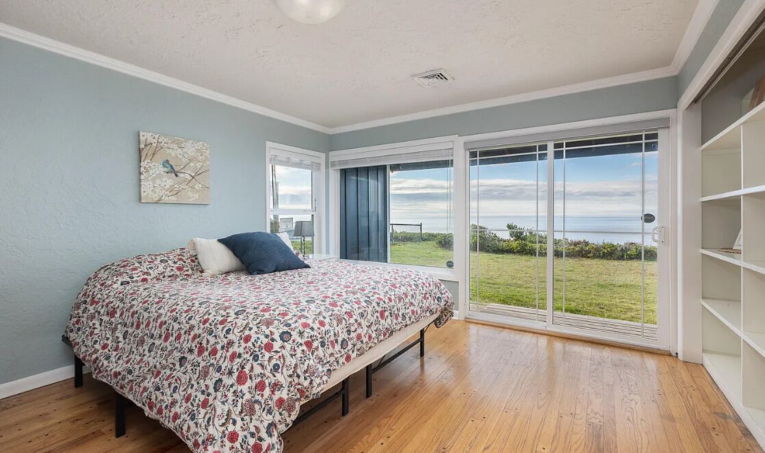 A bedroom with a large bed, a view of the outdoors through a sliding glass door, and a wall-mounted artwork.