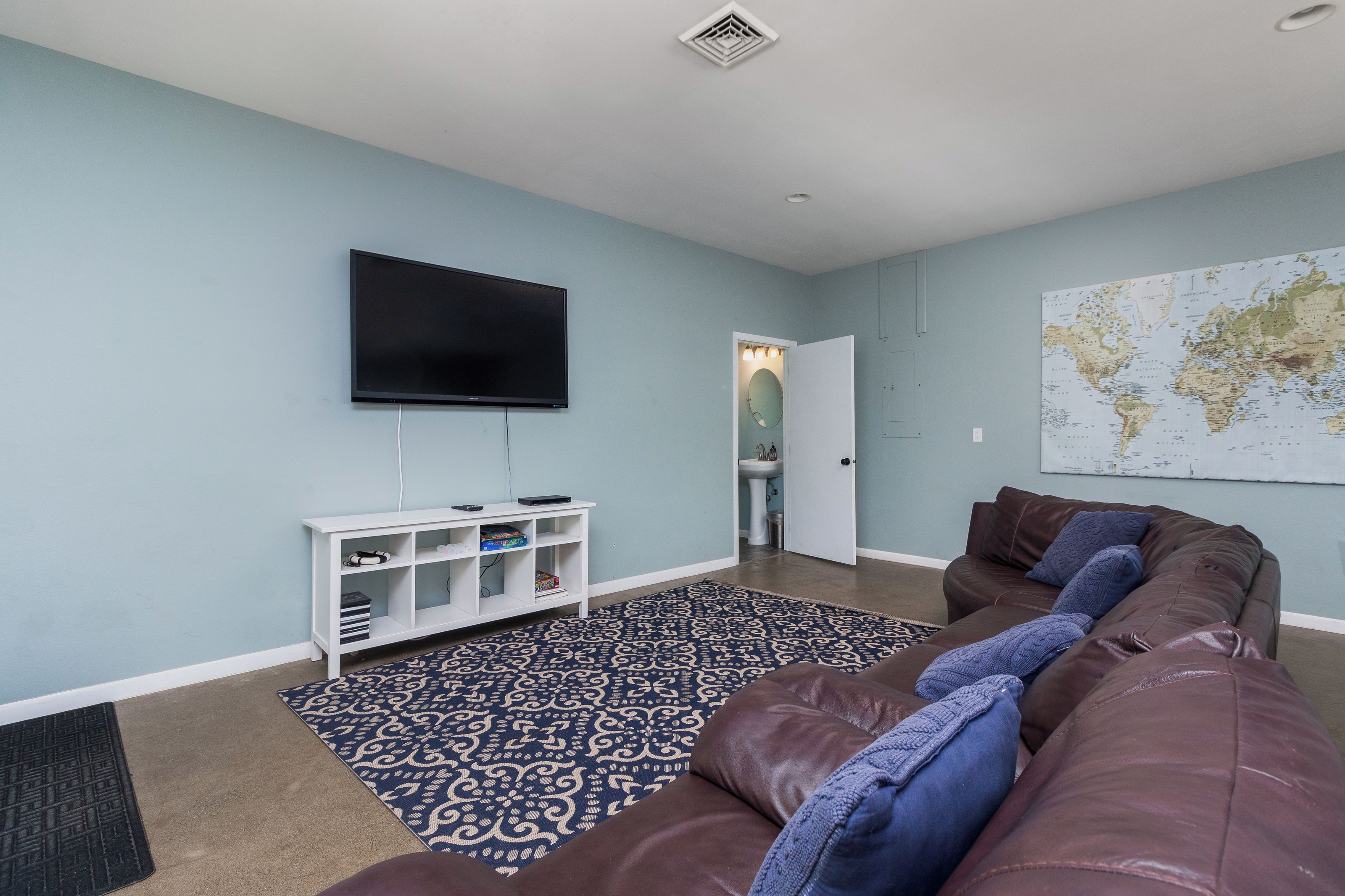 A living room with a flat-screen TV, a white entertainment unit, a patterned rug, a brown leather couch, and a world map on the wall.
