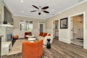 A spacious living area with a fireplace, a ceiling fan, and a view into the adjacent bathroom. - Private Pool + Guesthouse & Arcade | Tampa (Tampa)